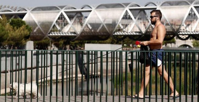 Un hombre pasea a su perro por una de las pasarelas de Madrid Río, que cruza el Manzanares paralela al icónico puente de Arganzuela, diseñado por el arquitecto francés Dominique Perrault, esta calurosa mañana de sábado de agosto. EFE/MARISCAL
