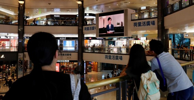 Varias personas escuchan el mensaje televisado de Carrie Lam en un centro comercial de Hong Kong. - REUTERS