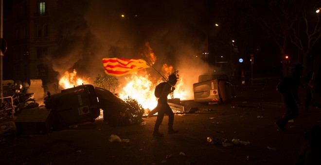 Un joven con una bandera estelada camina entre los contenedores en llamas en Barcelona. GUILLEM SANS
