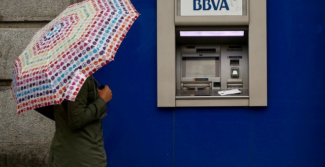 Una mujer con paraguas junto a un cajero automático de una sucursal de BBVA en Madrid. REUTERS/Andrea Comas