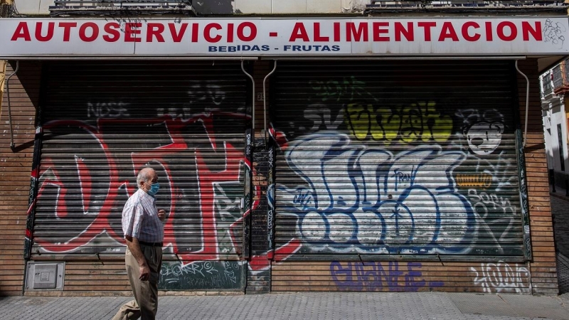 Un hombre protegido con mascarilla camina ante un comercio cerrado en una céntrica calle de Sevilla, durante el confinamiento decretado en el Estado de Alarma debido a la crisis sanitaria de la covid-19. EFE/Julio Muñoz