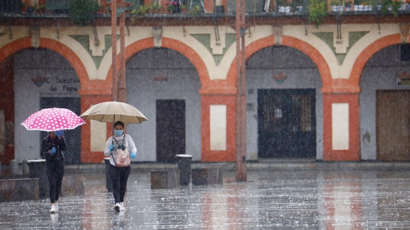 Dos mujeres con mascarillas y paraguas caminan por Córdoba. EFE/Salas