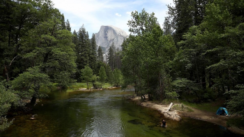 Un hombre nada en el río con la montaña Half Dome en la distancia en el Parque Nacional Yosemite, California, EEUU.- EZRA SHAW/AFP