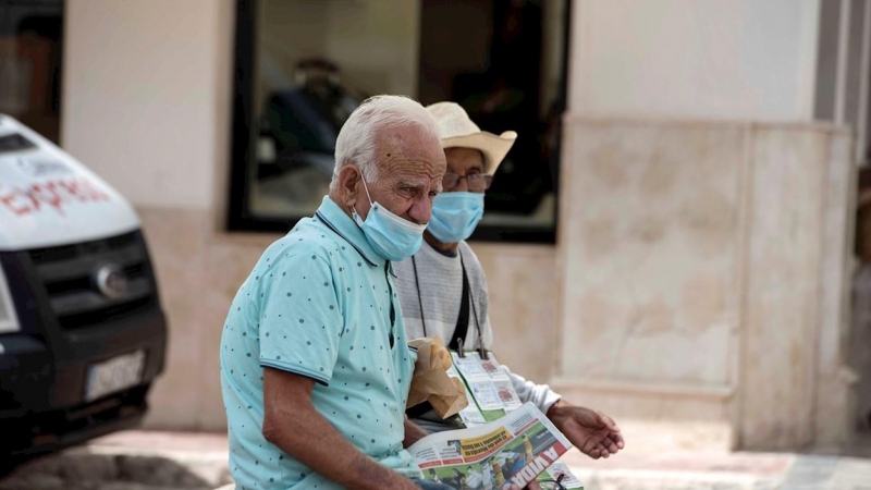 Una pareja de ancianos se protegen con mascarillas mientras descansan en un banco en Mahón, este jueves. | EFE