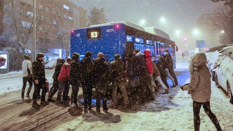 Varias personas empujan en Madrid un autobús atrapado por la nieve.