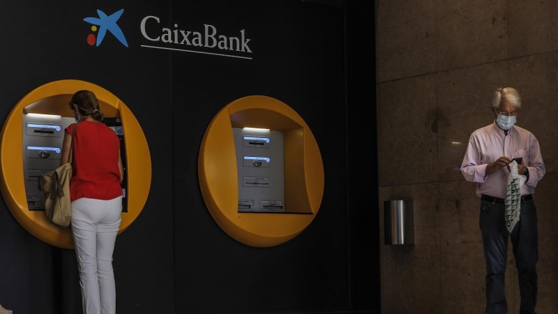 Dos personas en los cajeros dispuestos en el edificio de la sede de Caixabank, en Valencia. E.P./Rober Solsona