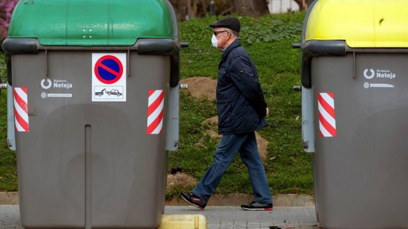 Un hombre camina junto a dos contenedores de basura.