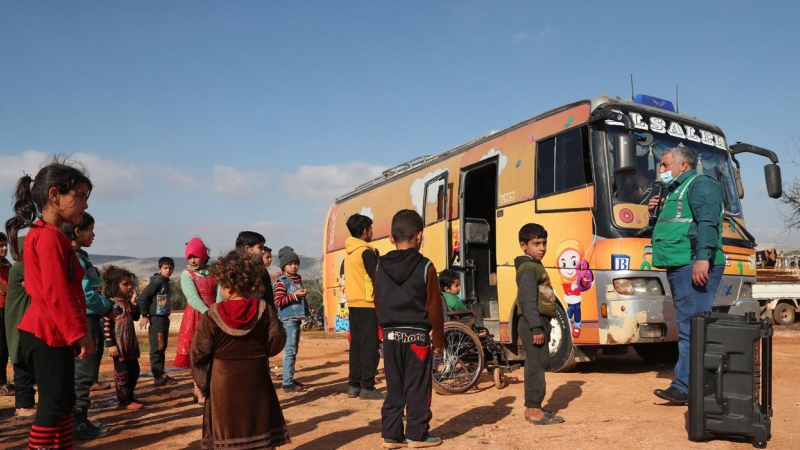 Un grupo de niños participa en una actividad al aire libre junto a un autobús especial utilizado como aula improvisada en el campamento de Haranbush para sirios desplazados en el norte de la provincia de Idlib, en el noroeste de Siria. Fotografía del 7 de