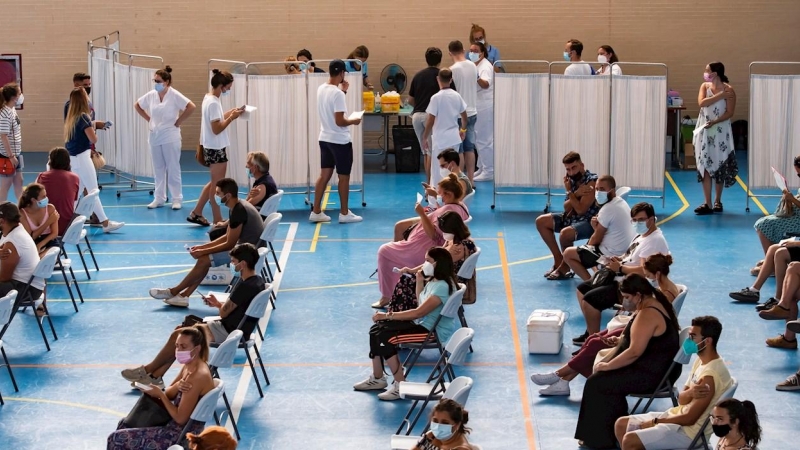 Multitud de jóvenes aguardan sentados tras recibir la vacuna contra el coronavirus en el pabellón municipal de Espartinas (Sevilla).