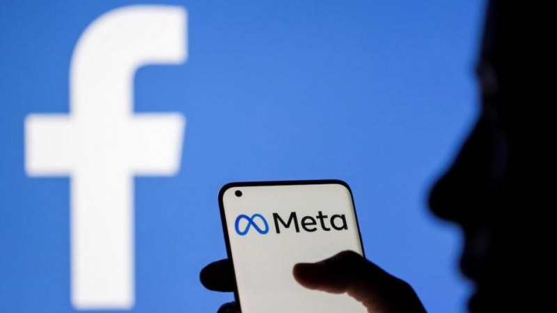 Una mujer sostiene un teléfono inteligente con el logotipo de Meta delante de la imagen de Facebook, a 28 de octubre de 2021.