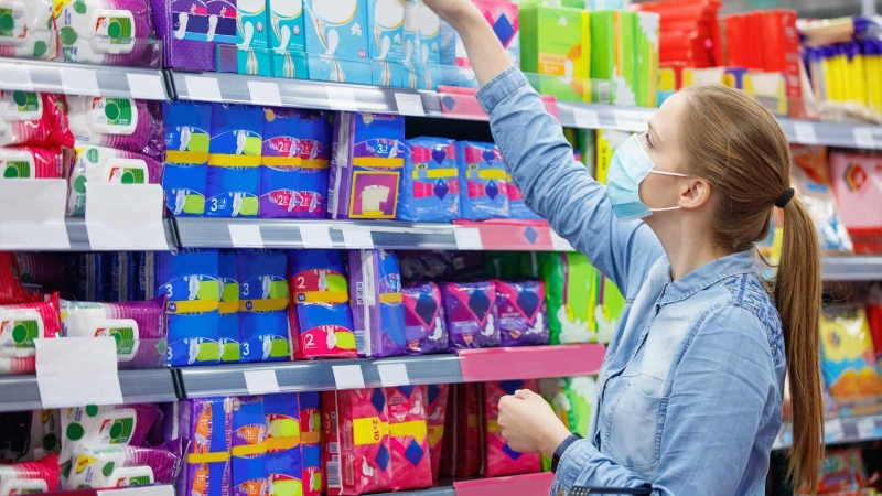 Una mujer escoge un paquete de compresas en un supermercado.