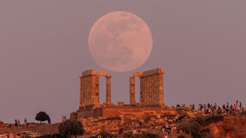 La gente ve una luna llena, conocida como la ' Luna de las Flores ', que se eleva detrás del Templo de Poseidón, antes de un eclipse lunar en el Cabo Sounion, cerca de Atenas, Grecia, el 15 de mayo de 2022.