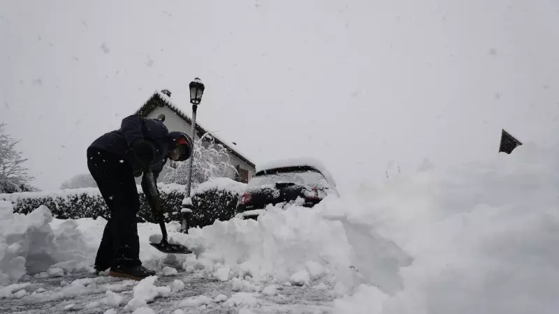 Una persona limpia la nieve para poder sacar su vehículo de una calle de Espinal (Navarra) donde una intensa nevada cubre completamente la carretera.