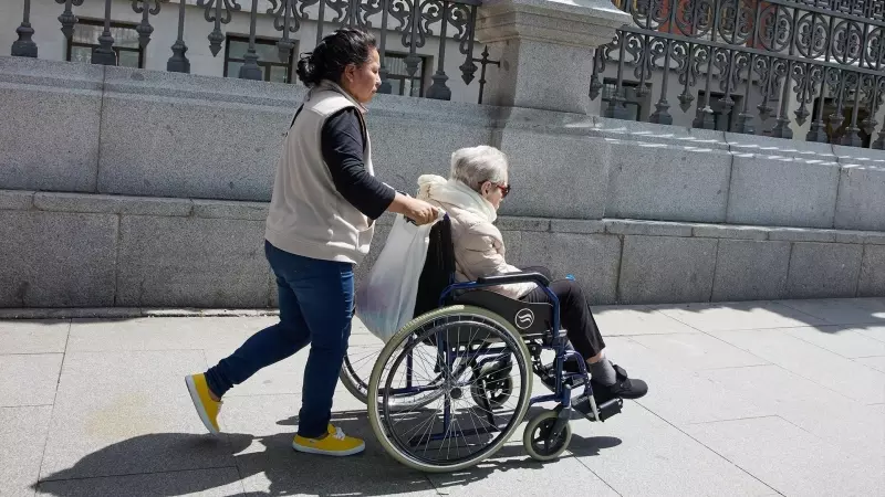 Una mujer mayor en silla de ruedas y su cuidadora pasean por el centro de la ciudad, a 4 de junio de 2023, en Madrid.