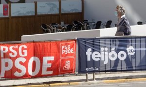 Una mujer protegida con mascarilla pasea junto a carteles electorales del PPdeG y del PSdeG en Foz, en la comarca de A Mariña, Lugo, (Galicia). / Europa Press
