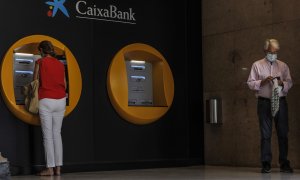 Dos personas en los cajeros dispuestos en el edificio de la sede de Caixabank, en Valencia. E.P./Rober Solsona