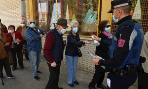 Un policía ofrece gel hidroalcohólico a votantes que esperan su turno para ejercer su derecho al voto en el Colegio Pinar del Rey en Madrid, este martes.
