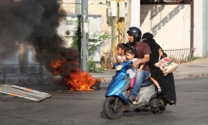 Una familia ocupa una moto mientras arden neumáticos cerca con motivo de las protestas por la explosión del año pasado ocurrida en el puerto, en Beirut. - REUTERS