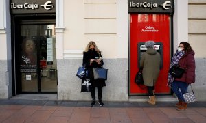 Una mujer utiliza el cajero automático de una oficina de Ibercaja en Madrid, mientras otras esperan. REUTERS/Juan Medina