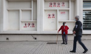 Dos personas mayores con mascarilla delante del Centro de Salud Pavones, donde hay carteles de protesta que rezan 'Urgencias Cerradas, tu salud vendida', a 21 de octubre de 2022, en Madrid.