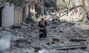 Una mujer palestina recorre una calle de la ciudad de Gaza cubierta de escombros por los bombardeos de la aviación israelí, que se mantienen por quinto día consecutivo.