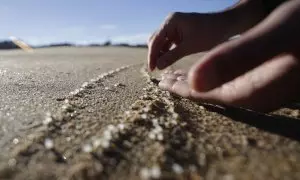 Una persona recoge pellets en la playa de Mera, situada en el concello coruñés de Oleiros, a 12 de enero de 2024.