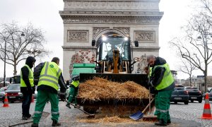 Los trabajadores municipales limpian paja arrojada por un tractor frente al Arco del Triunfo, en París, tras una protesta del sector agrario francés.