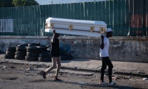 Dos hombres cargan un ataúd por una calle de Puerto Príncipe (Haití), tras los tiroteos.