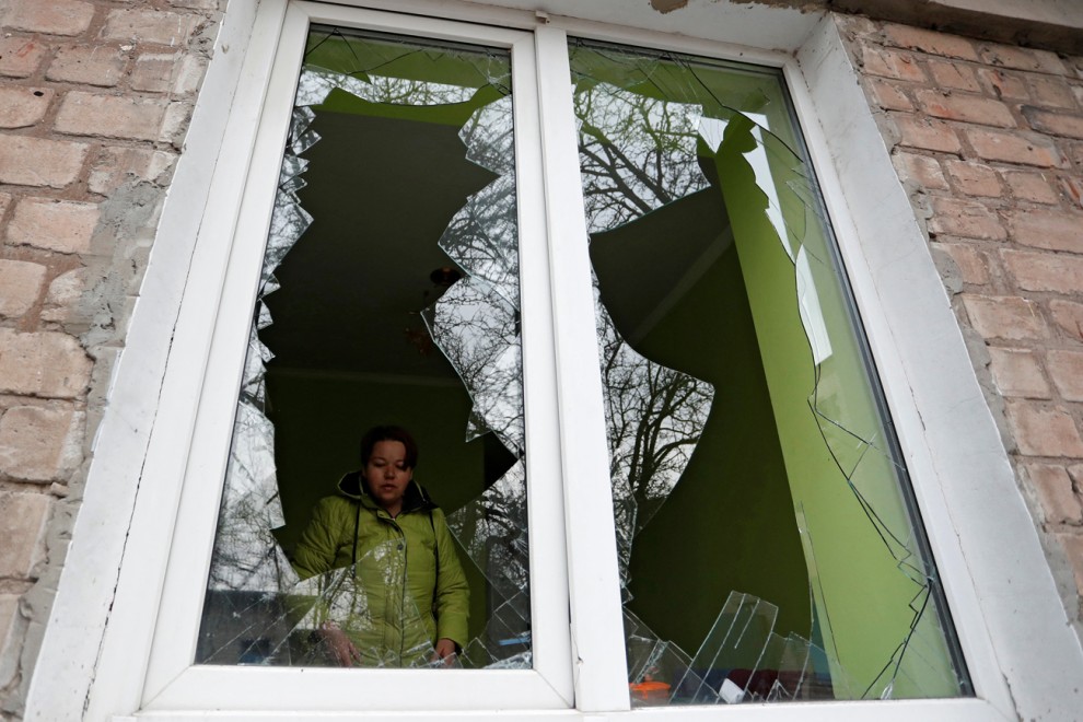 Una mujer mira a través de los cristales de su ventana, rotos por los recientes ataques bombardeos rusos en la ciudad de Yasynuvata (Yasinovataya), controlada por los separatistas prorusos, en la región de Donetsk.