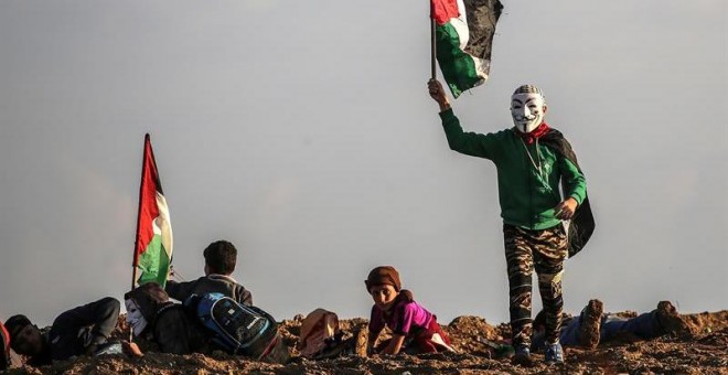 21/12/2018.- Un protestante palestino ondea una bandera nacional durante los enfrentamientos cerca de la frontera entre Israel y la Franja de Gaza, hoy, 21 de diciembre de 2018. Un menor palestino murió y doce resultaron heridos hoy por disparos del Ejérc