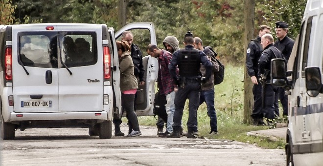 Gendarmes franceses llevan hasta unas furgonetas a los inmigrantes del campamento desalojado cerca del puerto de Dunkerque, en Francia.- AFP