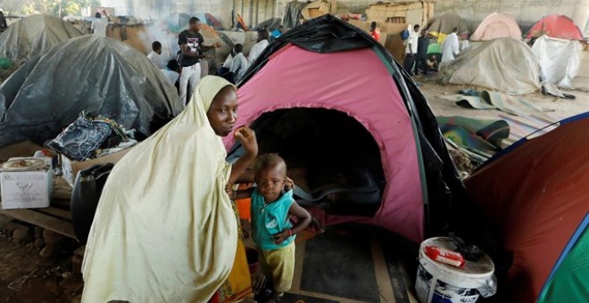 Una madre, junto a su hijo, en una acampada de personas migrantes. / Reuters