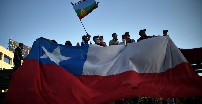 12/11/2019 - Manifestantes sostienen la bandera de Chile y la Mapuche. / AFP - RODRIGO ARANGUA