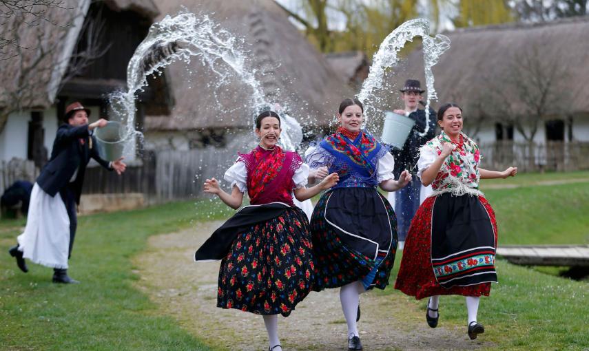 Tres mujeres corren mientras los hombres les lanzan agua, durante las celebraciones tradicionales de Pascua en Szenna (Hungría). / LASZLO BALOGH (REUTERS)