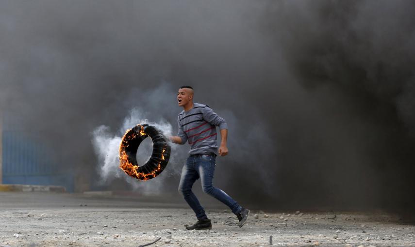 Un manifestante palestino, con un neumático en llamas durante un enfrentamiento con tropas israelíes, en protesta por los asentamientos judíos, en Jalazoun, cerca de la ciudad cisjordana de Ramala. /MOHAMAD TOROKMAN (REUTERS)