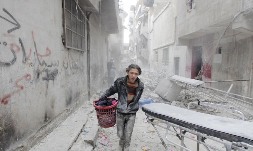 Un niño transporta sus pertenencias, en una calle afectada por lo que los activistas dijeron que fue una bomba de barril lanzada por las fuerzas leales a Al Assad, en Alepo (Siria). /RAMI ZAYAT (REUTERS)