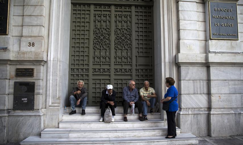 La gente se sienta en la puerta de una sucursal del Banco Nacional de Grecia, cerrado tras el corralito por el anuncio del referedum sobre las medidas propuestas por los acreedores de la deuda griega.- REUTERS / Marko Djurica