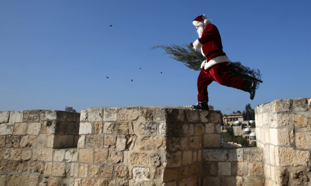 Un palestino cristiano vestido de Papá Noel camina con un árbol de Navidad a lo largo de los muros viejos de la ciudad de Jerusalén mientras los cristianos de todo el mundo se preparan para celebrar la Navidad. AFP/GALI Tibbon