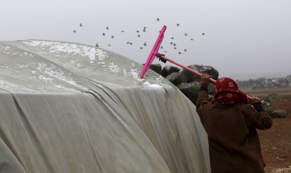 Una mujer quita la nieve y el agua de la parte superior de una tienda de campaña en el campamento Jerjnaz para refugiados, en la provincia de Idlib.  REUTERS/Khalil Ashawi