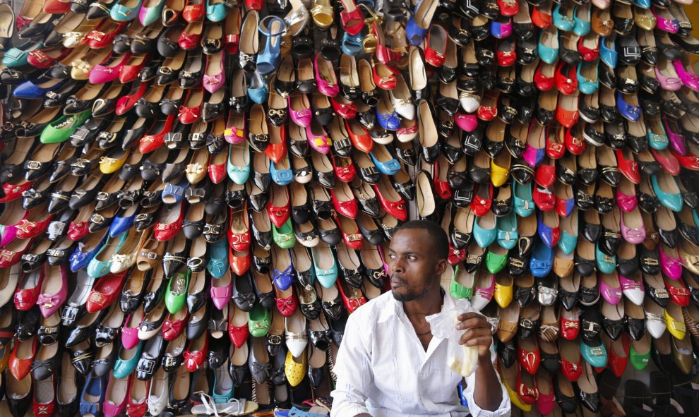 Un vendedor permanece sentado delante de cientos de zapatos en su tienda de Kampala, Uganda. EFE/Dai Kurokawa