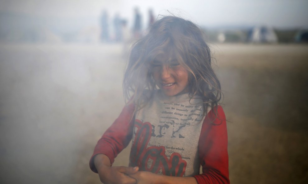 Una niña entre humo en un campamento improvisado para refugiados en la frontera entre Grecia y Macedonia, cerca de la localidad de Idomeni. REUTERS/Marko Djurica