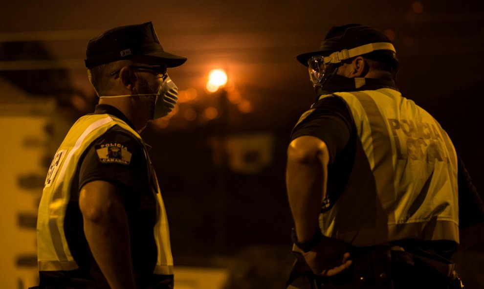 Dos miembros de la policía hacen guardia mientras el fuego se aproxima, en Las Manchas, al suroeste de la isla de La Palma. REUTERS/Borja Suarez