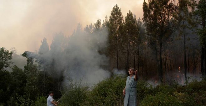 Dos habitantes de Louriceira intentan apagar un foco cerca de su pueblo. | MIGUEL VIDAL (EFE)