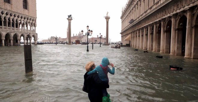 Una mujer sostiene a una niña mientras camina en una inundada plaza de San Marcos. Reuters / Manuel Silvestri