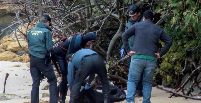 La Guardia Civil junto a uno de los dos cadáveres más hallados de los ocupantes de la patera que naufragó el pasado lunes en la playa de Caños de Meca (Cádiz), mientras que la Policía ha detenido al patrón de la embarcación y a su ayudante, quienes cobrar