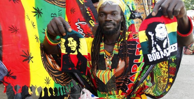 Un miembro del grupo musical Ivoire Binghi muestra banderas con la cara del músico jamaicano Bob Marley en una calle de Abiyán (Costa de Marfil). / EFE