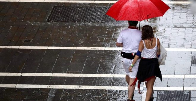 Dos personas se protegen de la lluvia en una de las céntricas calles de Pamplona durante la fiesta de San Fermín. Navarra está en alerta amarilla este lunes por lluvias y tormentas, según Aemet. EFE/ Javier Lizón