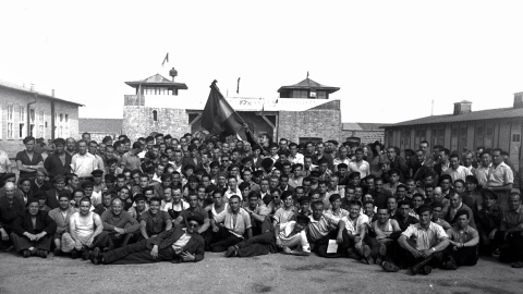 Grupo de españoles después de la liberación, con la pancarta en la que saludan a las tropas de liberación sobre la puerta de acceso al campo. Juan está en el centro de la imagen.- DEPORTADOS.ES