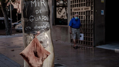 Una persona pasa ante la Consellería de Sanidad donde se puede ver una bolsa de basura usada a modo de bata con el lema "MIR de guardía ¿Te atiendo?". EFE/Biel Aliño