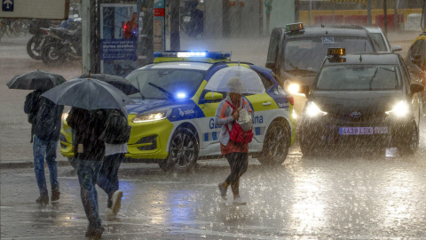 Varias personas se protegen de la lluvia en la Plaza de Espanya de Barcelona.